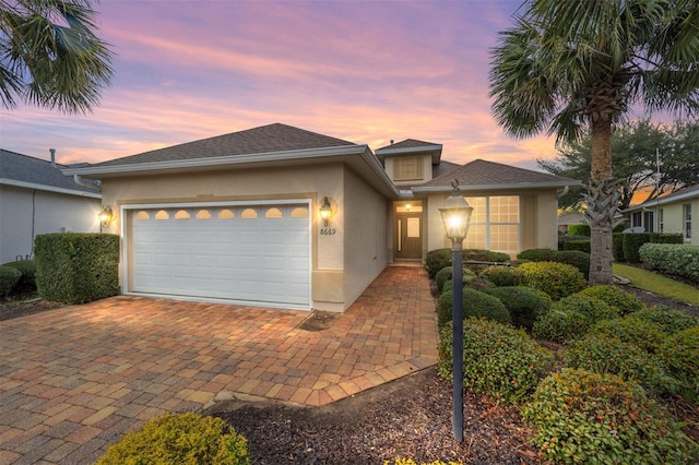 view of front of property featuring an attached garage, a shingled roof, decorative driveway, and stucco siding