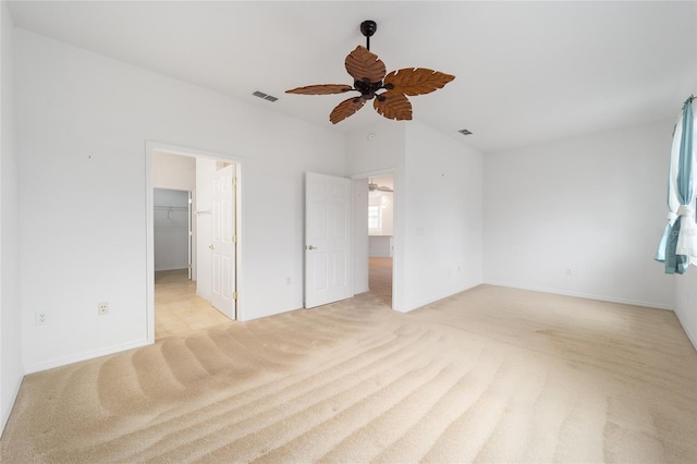 unfurnished bedroom with visible vents, baseboards, light colored carpet, ceiling fan, and a walk in closet