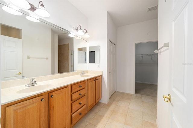 bathroom with a sink, visible vents, tile patterned floors, double vanity, and a walk in closet