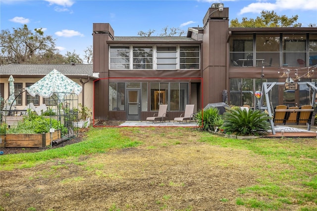 rear view of house with a patio area, a garden, a chimney, and a yard