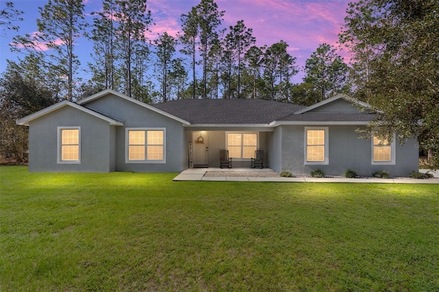 view of front of property featuring roof with shingles, a lawn, and stucco siding