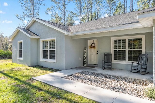 exterior space featuring stucco siding, a shingled roof, and a front yard