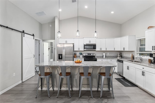 kitchen featuring stainless steel appliances, a barn door, a kitchen island, a sink, and high vaulted ceiling