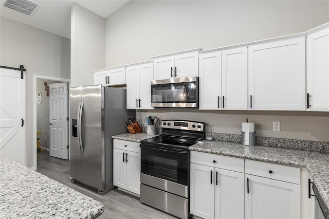 kitchen with visible vents, a barn door, appliances with stainless steel finishes, light wood-style floors, and white cabinets