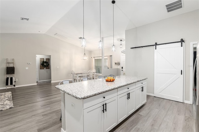 kitchen with vaulted ceiling, a barn door, light wood-type flooring, and visible vents