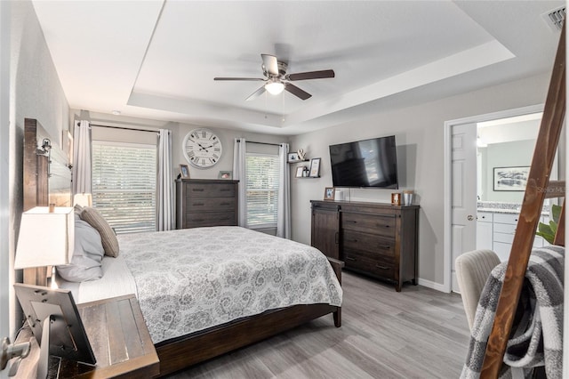 bedroom with light wood finished floors, a raised ceiling, visible vents, ceiling fan, and baseboards