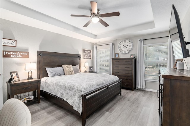 bedroom featuring light wood finished floors, ceiling fan, a tray ceiling, and baseboards