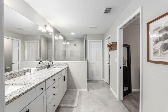 full bath with double vanity, visible vents, a sink, a textured ceiling, and tiled shower