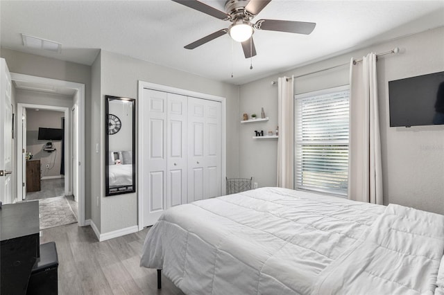 bedroom with wood finished floors, visible vents, baseboards, a ceiling fan, and a closet