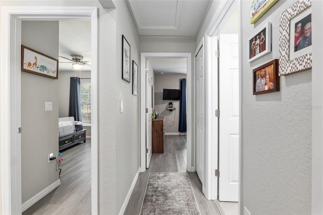 hall featuring a textured wall, baseboards, and wood finished floors