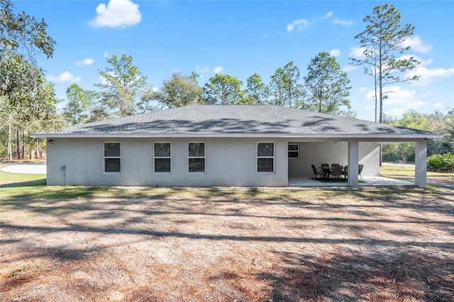 rear view of property with a shingled roof, a patio area, and stucco siding