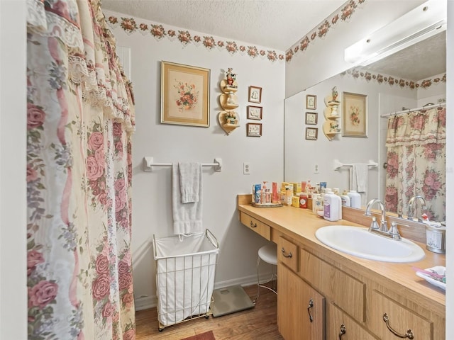 full bath with a shower with shower curtain, a textured ceiling, vanity, wood finished floors, and baseboards