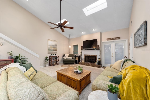 living room featuring light tile patterned floors, a skylight, a ceiling fan, high vaulted ceiling, and a high end fireplace