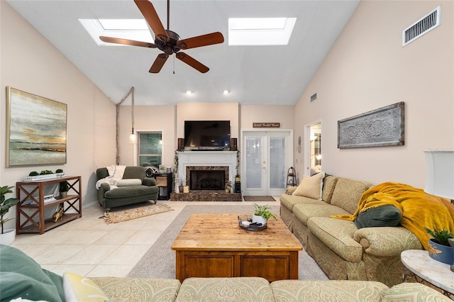 living area featuring light tile patterned floors, a fireplace with raised hearth, a skylight, visible vents, and a ceiling fan