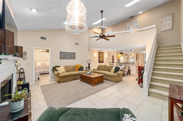 living area with light tile patterned floors, a ceiling fan, stairway, a fireplace, and high vaulted ceiling