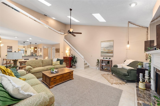 living area featuring high vaulted ceiling, light tile patterned flooring, a fireplace, a skylight, and stairway