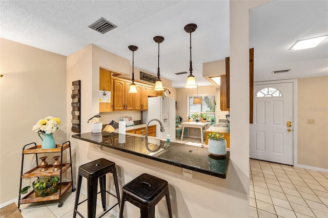 kitchen with light tile patterned floors, a peninsula, white refrigerator with ice dispenser, and visible vents