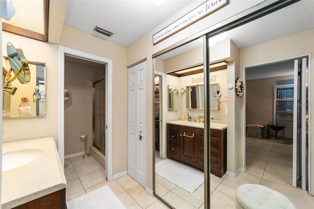 full bathroom with a textured ceiling, a shower with shower door, vanity, visible vents, and tile patterned floors