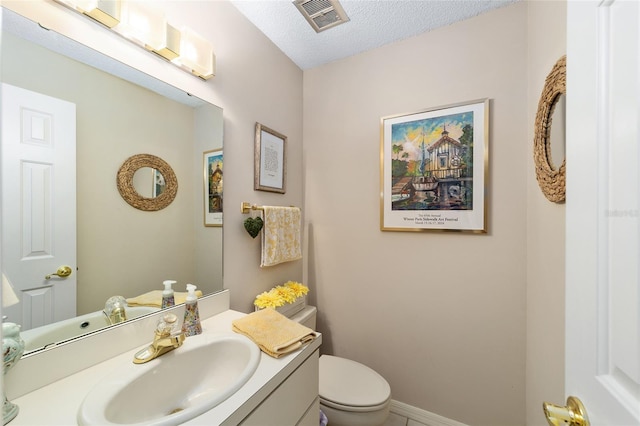 half bath featuring baseboards, visible vents, toilet, a textured ceiling, and vanity