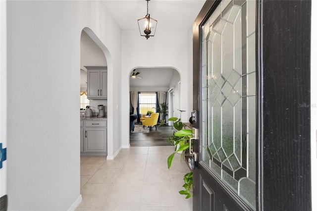 foyer featuring arched walkways, light tile patterned flooring, and baseboards