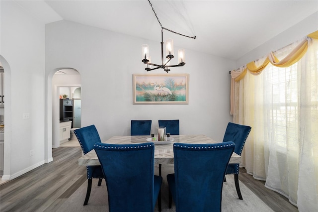 dining room featuring arched walkways, lofted ceiling, wood finished floors, a chandelier, and baseboards