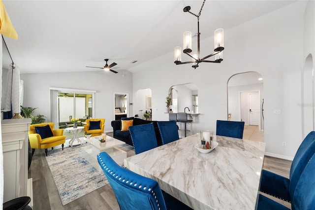 dining space with arched walkways, vaulted ceiling, and wood finished floors