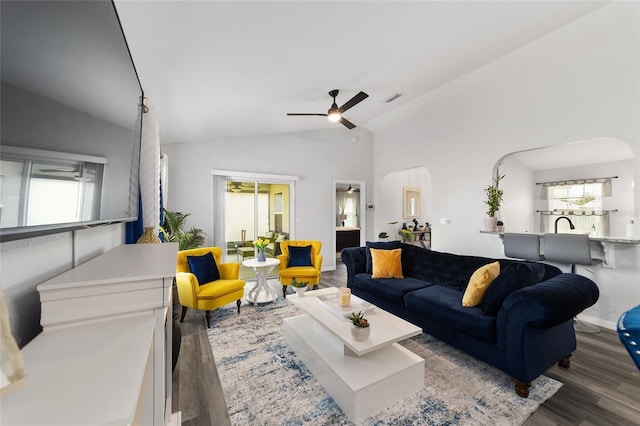 living area featuring arched walkways, visible vents, a ceiling fan, vaulted ceiling, and wood finished floors