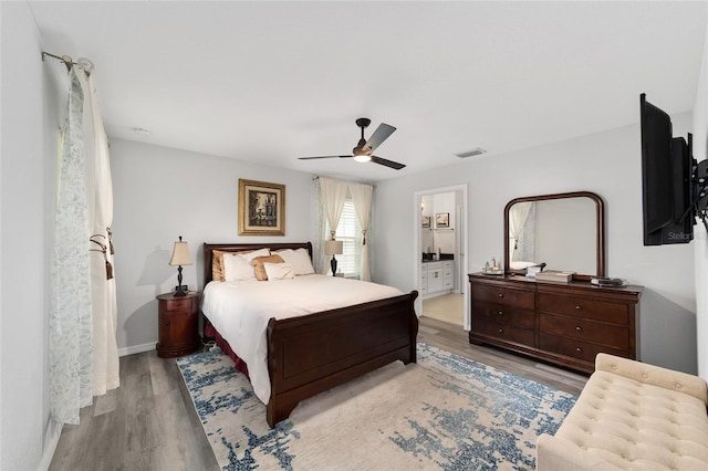 bedroom featuring wood finished floors, visible vents, baseboards, a ceiling fan, and ensuite bath