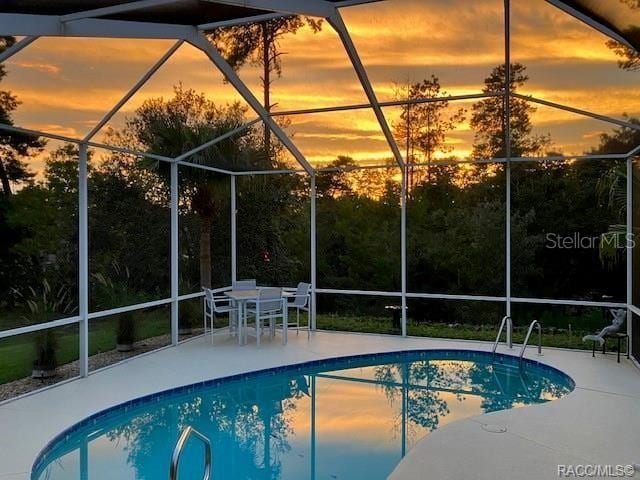 pool at dusk featuring a lanai, an outdoor pool, and a patio