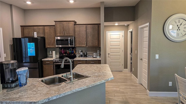 kitchen featuring dark brown cabinetry, baseboards, light wood-style flooring, stainless steel appliances, and a sink