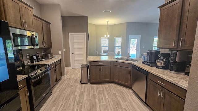 kitchen with light stone counters, pendant lighting, stainless steel appliances, light wood-style floors, and a sink