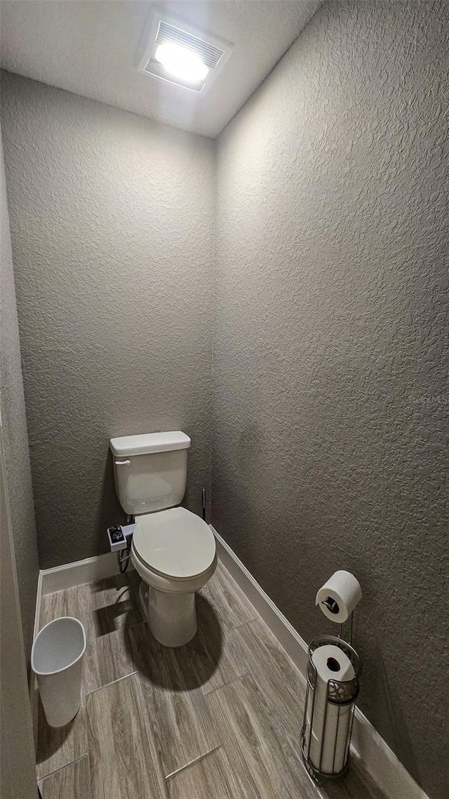 bathroom with visible vents, baseboards, a textured wall, toilet, and wood tiled floor