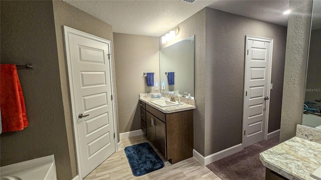 full bathroom with baseboards, two vanities, a sink, and a textured wall