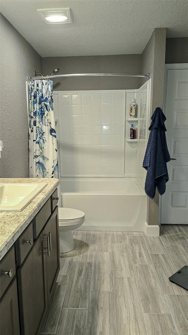 full bath featuring a textured wall, toilet, shower / bath combo with shower curtain, a textured ceiling, and vanity