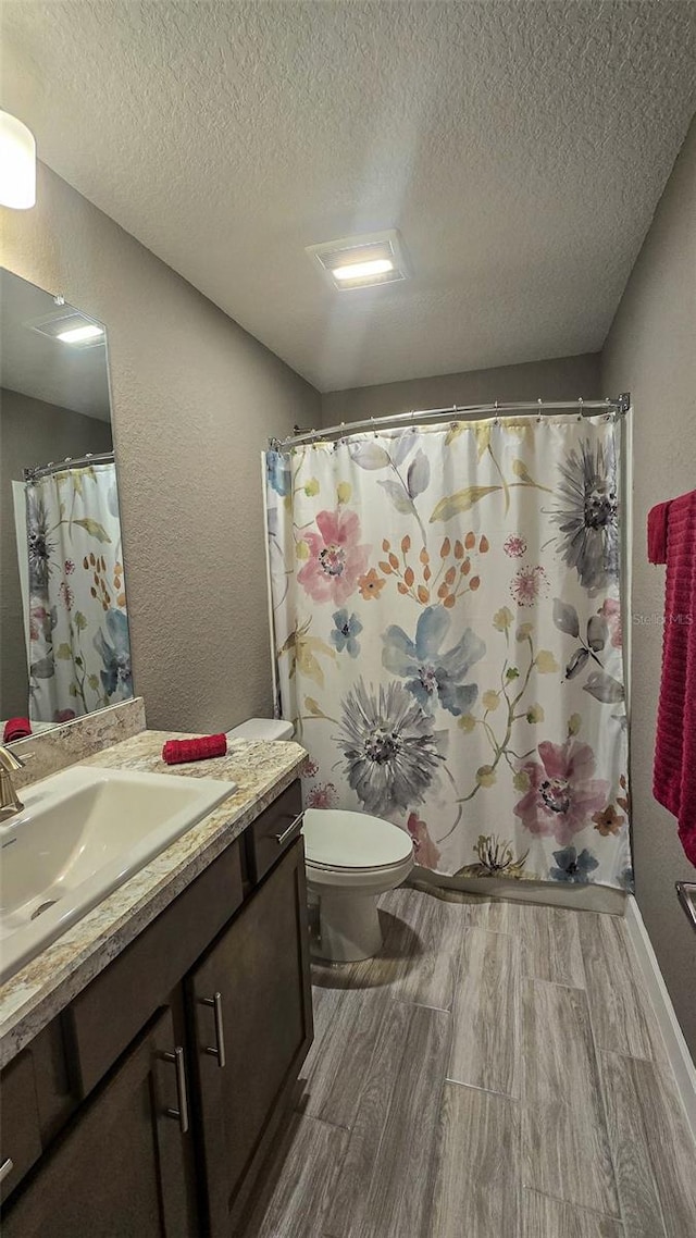 full bathroom featuring a textured wall, toilet, a textured ceiling, vanity, and wood finished floors