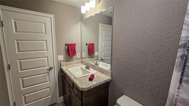 bathroom featuring a textured wall, vanity, and toilet