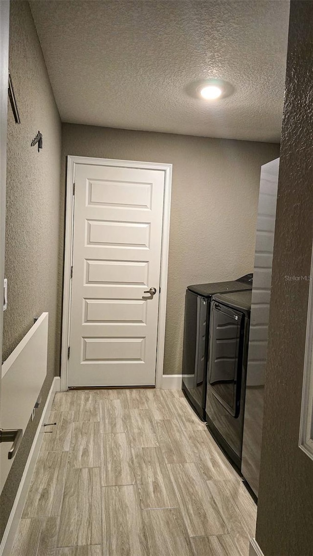 laundry area featuring laundry area, a textured wall, independent washer and dryer, a textured ceiling, and light wood-style floors