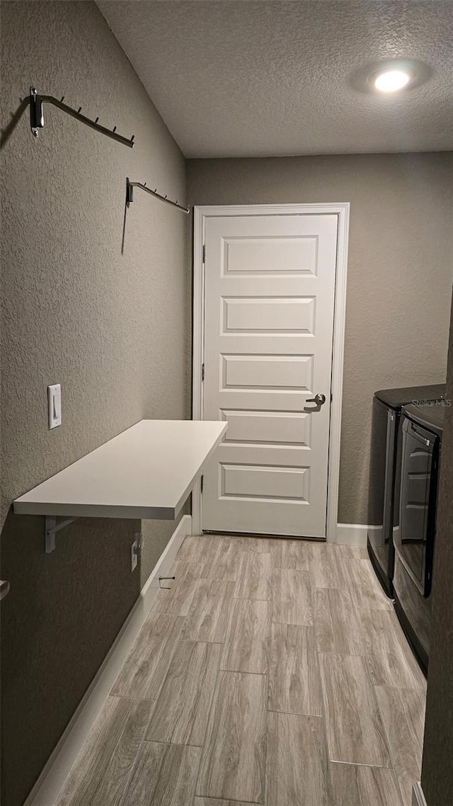 interior space with laundry area, a textured wall, light wood finished floors, and separate washer and dryer