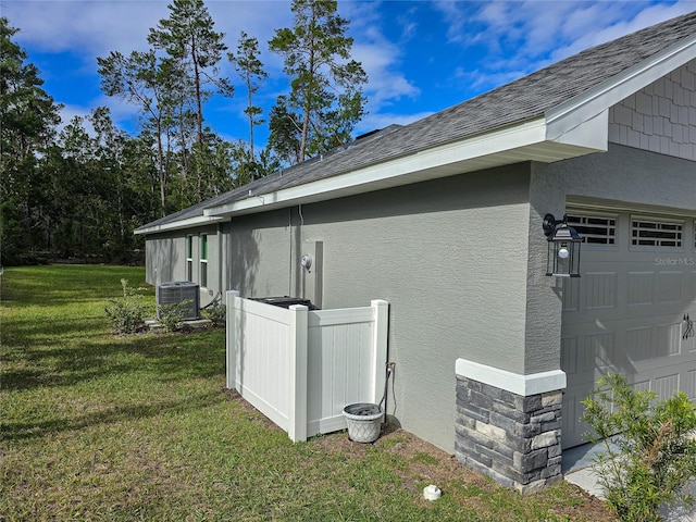 view of side of property with a shingled roof, stone siding, a yard, central air condition unit, and stucco siding