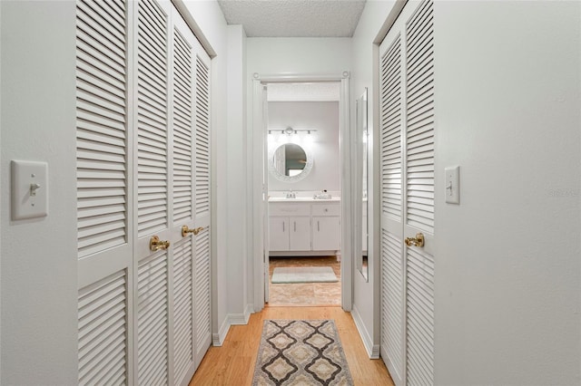 hallway with light wood-style floors, a textured ceiling, and baseboards