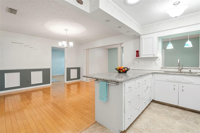 kitchen featuring pendant lighting, visible vents, open floor plan, white cabinets, and a sink