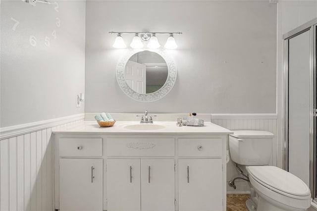 full bath with wainscoting, a shower with door, vanity, and toilet