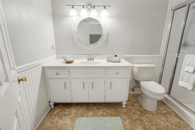 bathroom with a wainscoted wall, toilet, a shower stall, and vanity