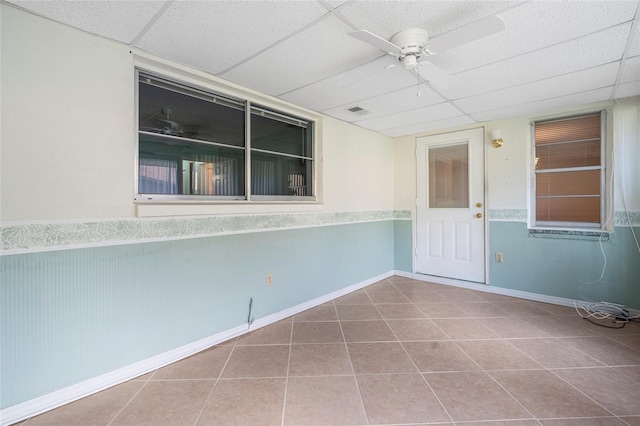 tiled empty room with a paneled ceiling, a ceiling fan, and wainscoting