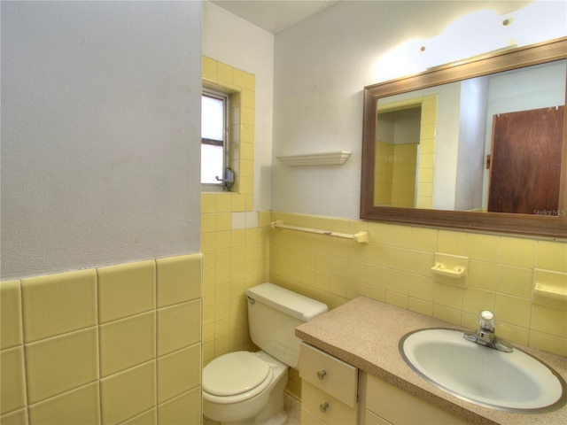 bathroom with toilet, a wainscoted wall, tile walls, and vanity