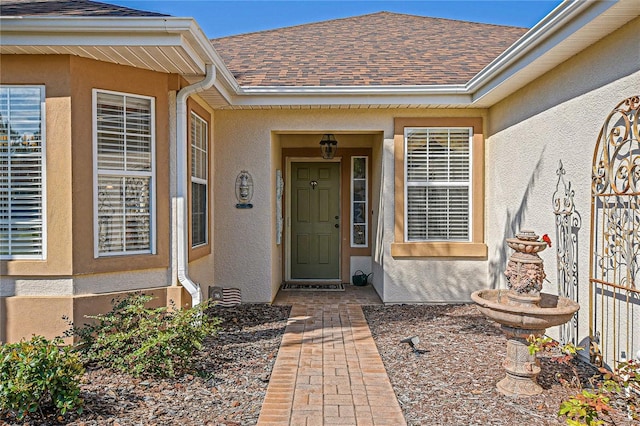 view of exterior entry with roof with shingles and stucco siding