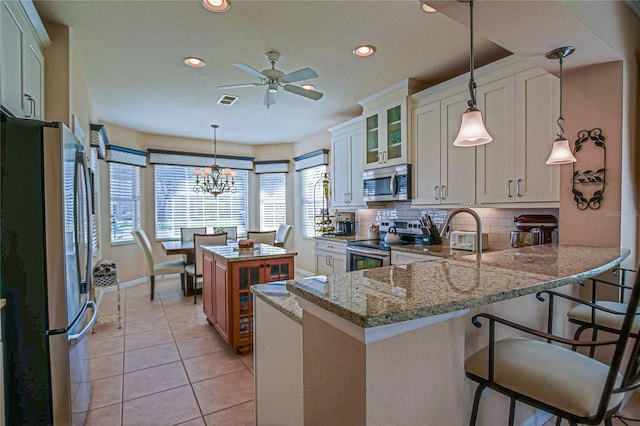 kitchen with light tile patterned floors, light stone counters, stainless steel appliances, a peninsula, and tasteful backsplash