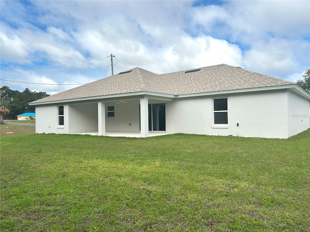 rear view of house with a shingled roof, stucco siding, a patio, and a lawn