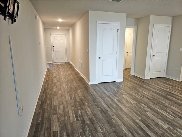 hallway with dark wood-style flooring, visible vents, and baseboards