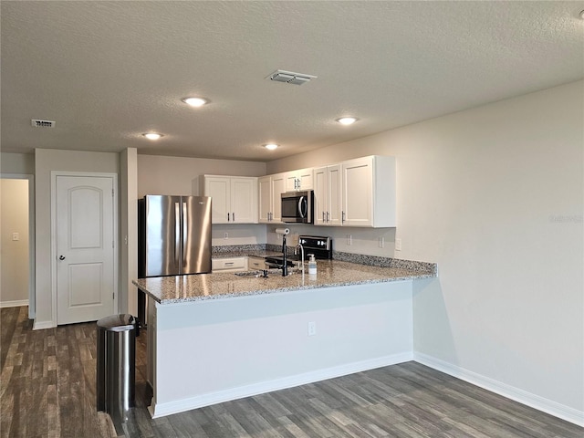 kitchen featuring light stone counters, stainless steel appliances, a peninsula, visible vents, and white cabinetry